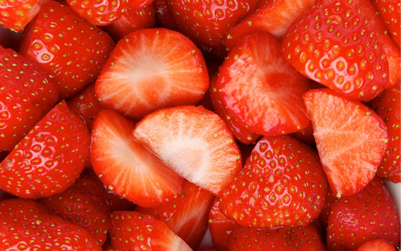 Close-up image of fresh strawberries, some whole and others cut in half, revealing their juicy red flesh and small seeds. Amid winter blahs, their vibrant hues offer a burst of color and energy to any dreary day, capturing an appetizing and lively appearance in every glossy detail.